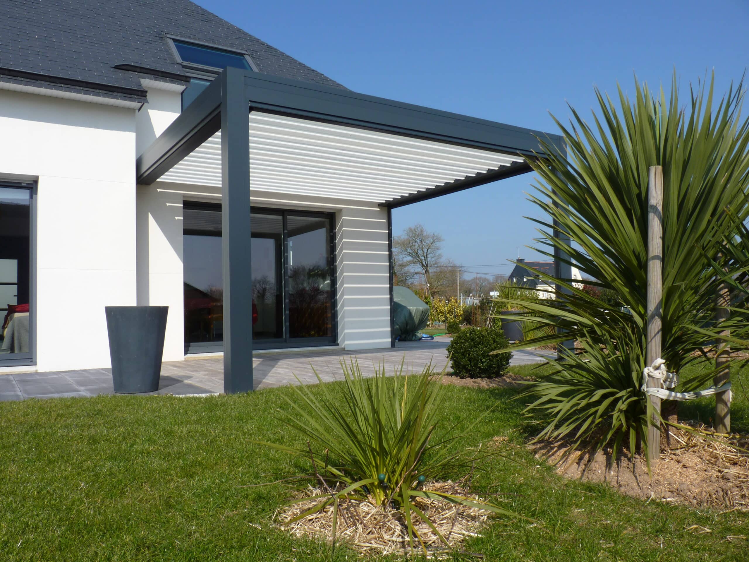 Pergola bioclimatique attenante à la maison avec deux piliers de support et lames orientables